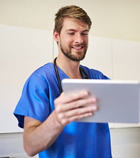 smiling male nurse in a blue scrub looking at the tablet