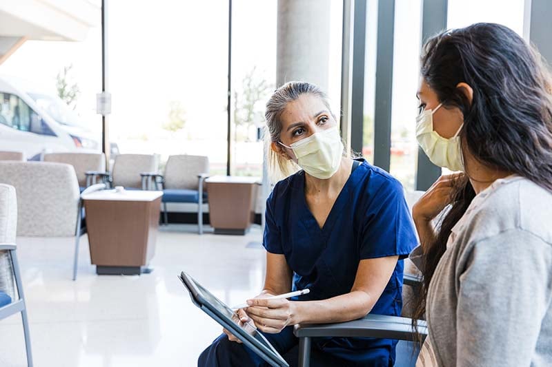 Nurse in face mask holding tablet helps patient in face mask