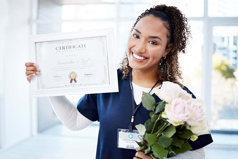 A smiling nurse holds up a diploma.