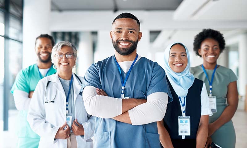 A group of culturally diverse health care workers are smiling and standing in a group and facing forward.