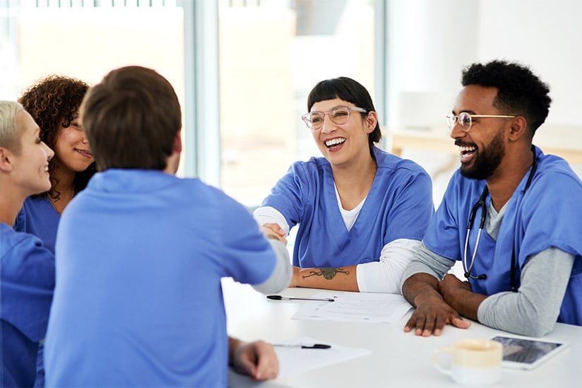 Group of laughing medical practitioners laugh together at a table.