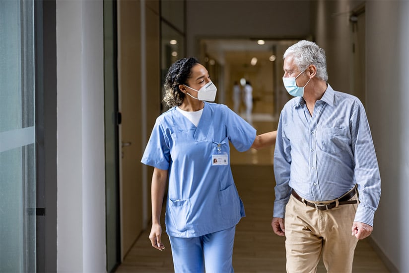 Female medical practitioner walks along a hallway with a older man.