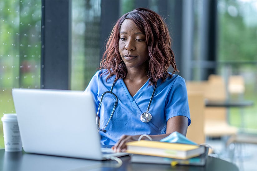 African American female nurse seated at a table and studying for her case management exam on her laptop.